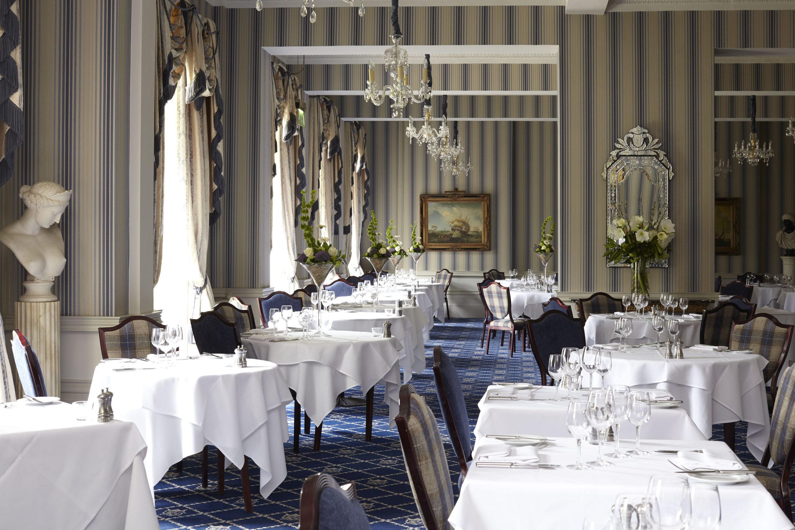 Elegant restaurant dining room with white tablecloths, chandeliers and set tables.
