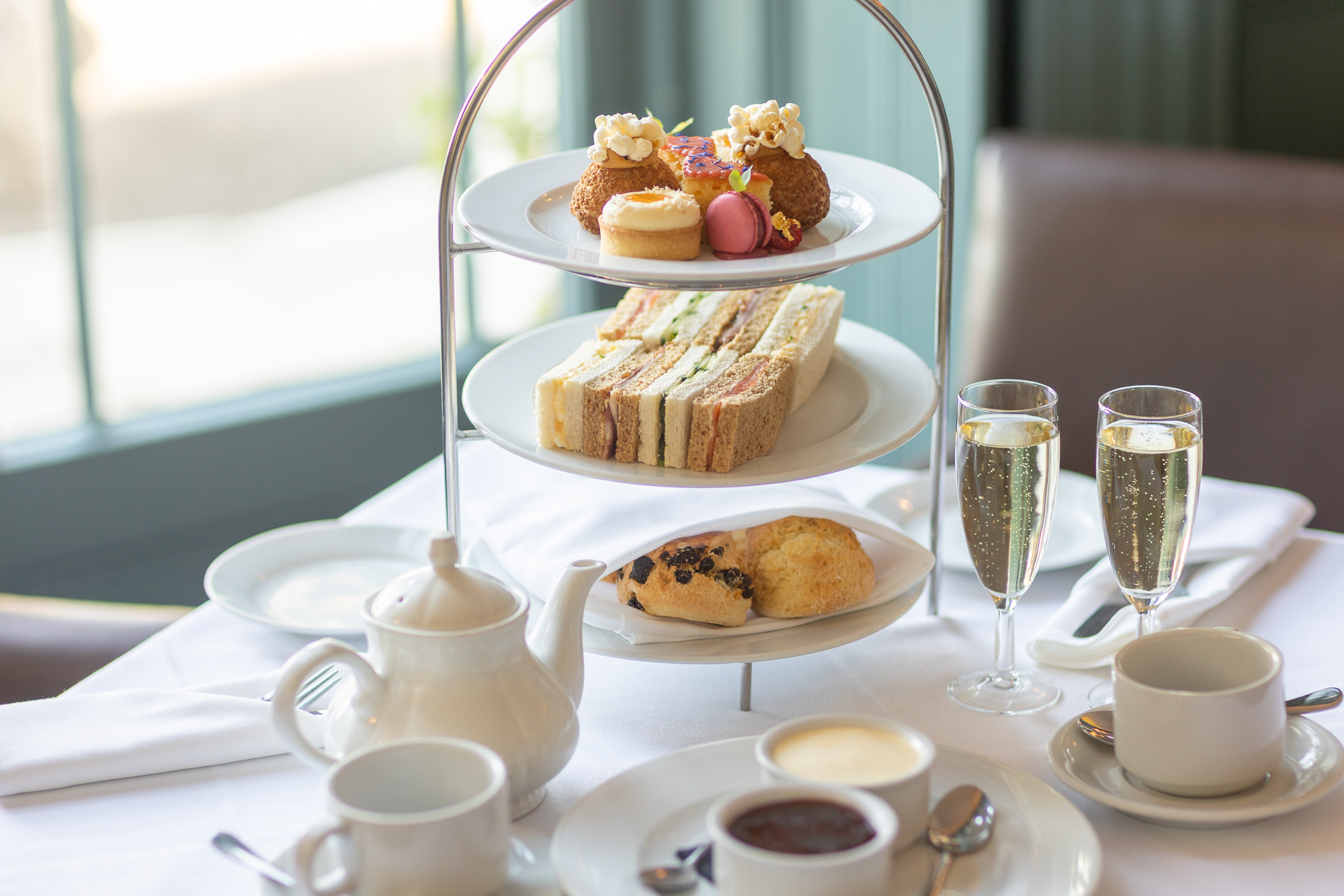 Afternoon tea stand with sandwiches, cakes, scones and glasses of sparkling wine.