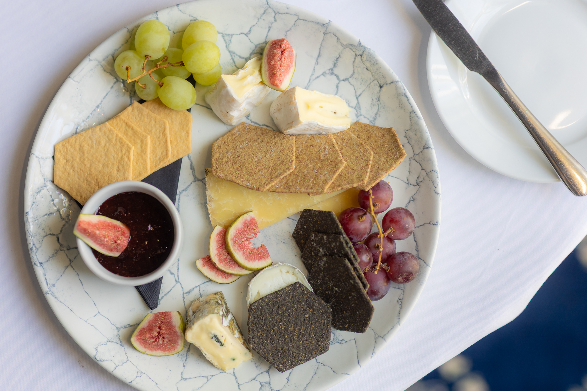 Cheeseboard with crackers, grapes, figs and chutney served on a patterned plate.