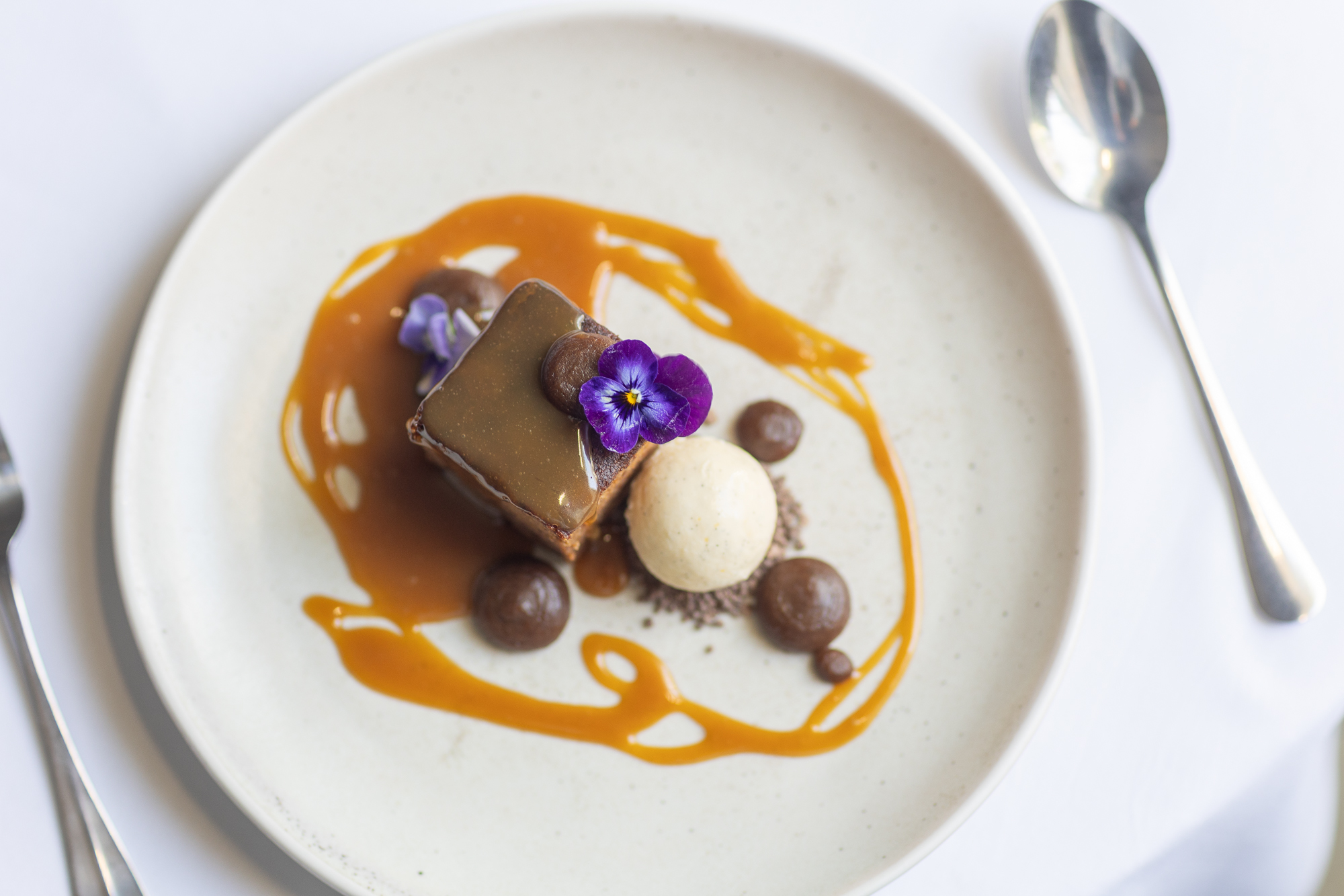 Plated dessert with caramel sauce, ice cream and edible flowers.