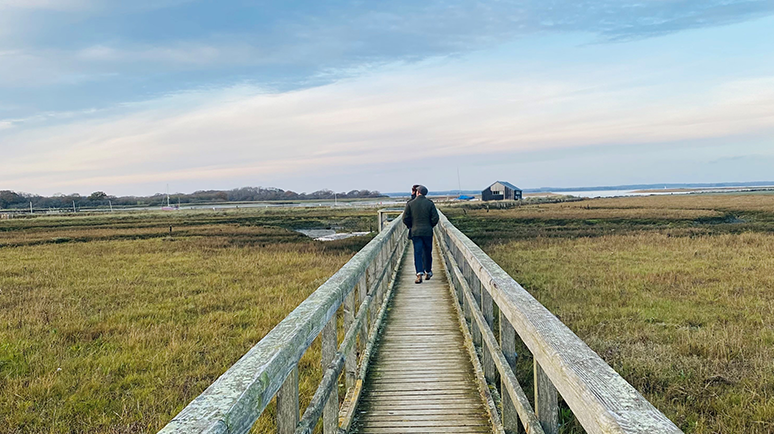 Two walkers on a cloudy but bright day walking down the wooden pathway across NEwtown Nature Reserve, Isle of Wight