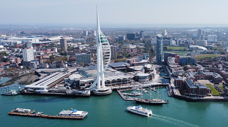 Aerial shot of white Spinnaker Tower towering over Portsmouth Harbour. A Wightlink FastCat is approaching the tower in the water.