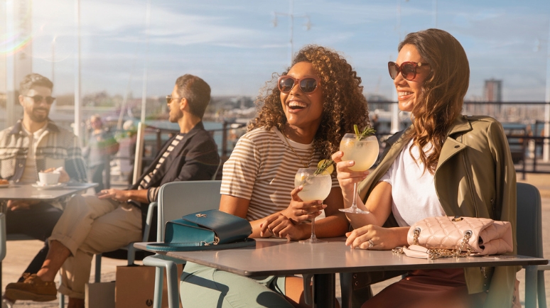 Two women at a restaurant table in Gunwharf Quays share a joke over a drink