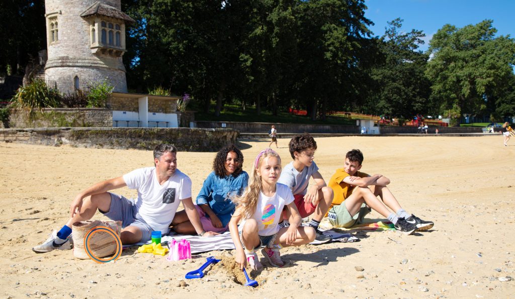 A family sitting on a sandy beach, Appley on the Isle of Wight, in front of Appley Tower