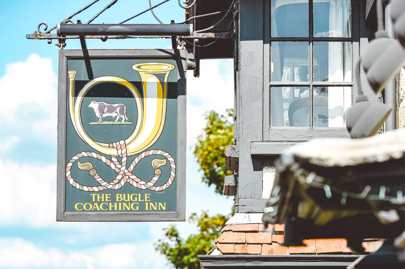 A pub sign which says 'The Bugle Coaching Inn'. Youc an also see a small portion of the pub's upper windows