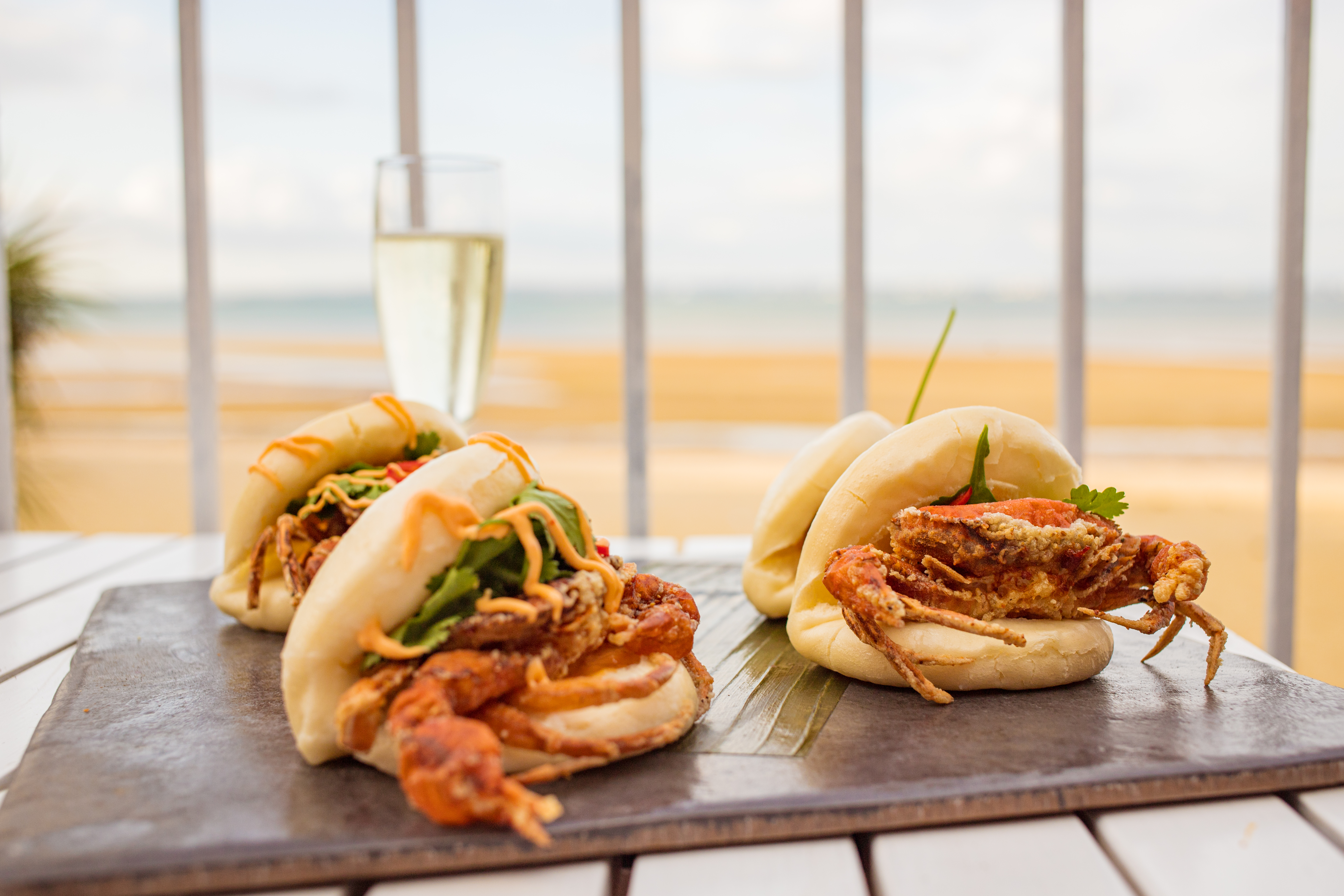 A slate of Bao buns and a glass of bubbly on a table overlooking the beach at Cadet Beach Club, Ryde, Isle of Wight