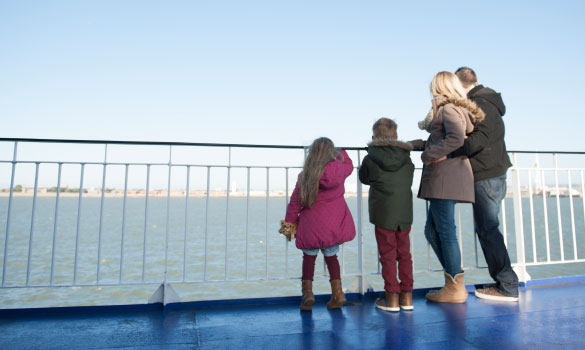 A family - two adults and two children - on a blue boat deck looking out to sea