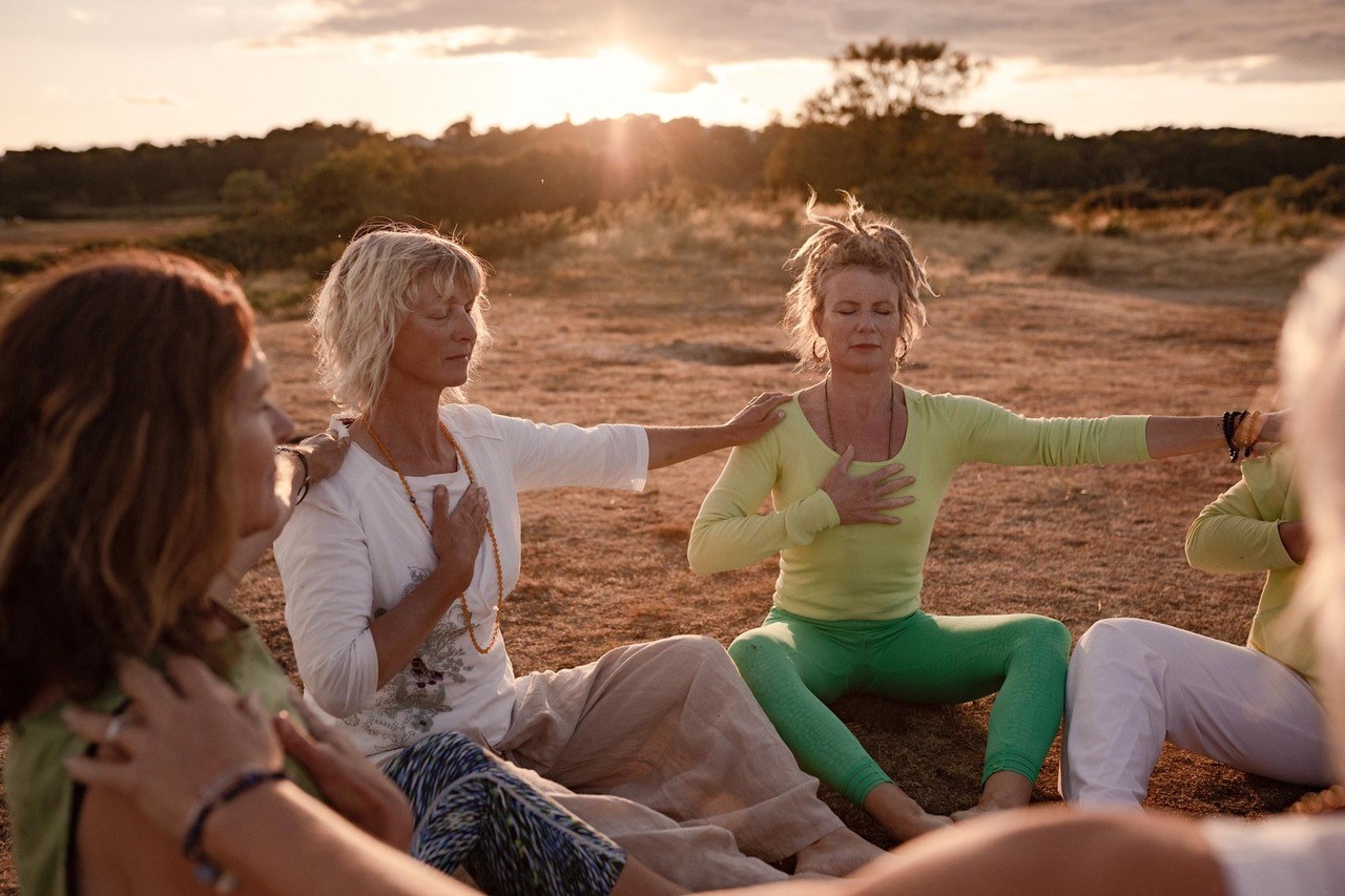A group women doing yoga in a circle, seated on the ground, in the countryside of the Isle of Wight