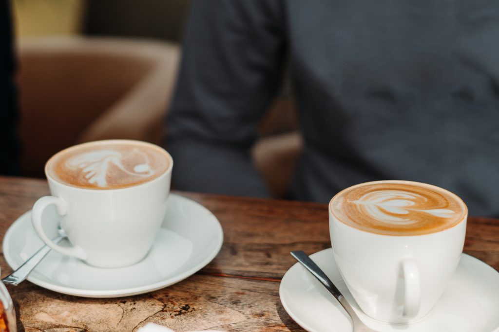 Two cups of coffee at a table with a person in the background