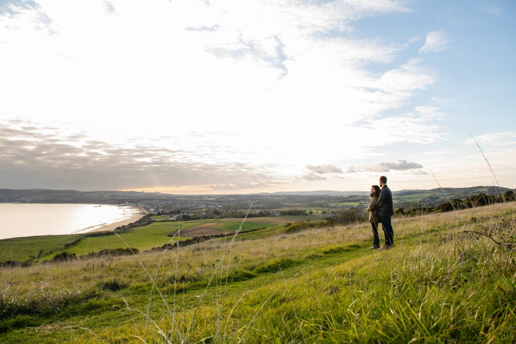 A couple standing on a grassy hill overlooking the coast of the Isle of Wight