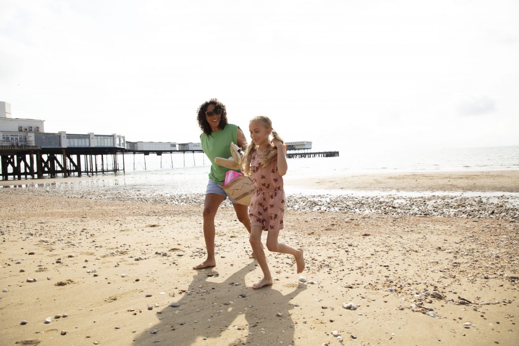 A woman and a girl on a sandy beach at Shanklin, Isle of Wight, with a pier in the background