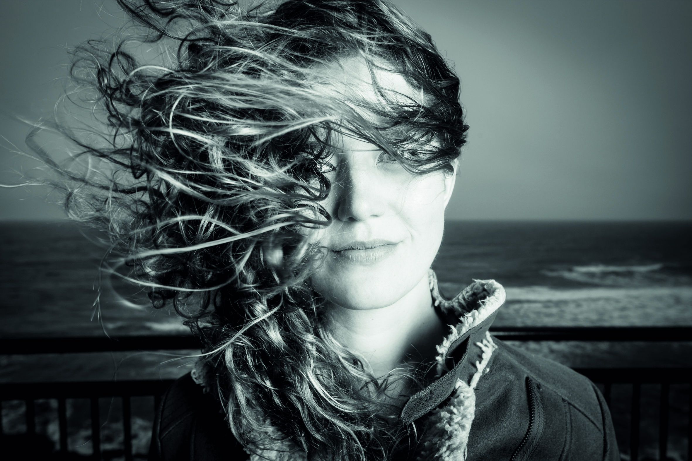 A portrait of Hannah George with her hair blowing on a windswept beach