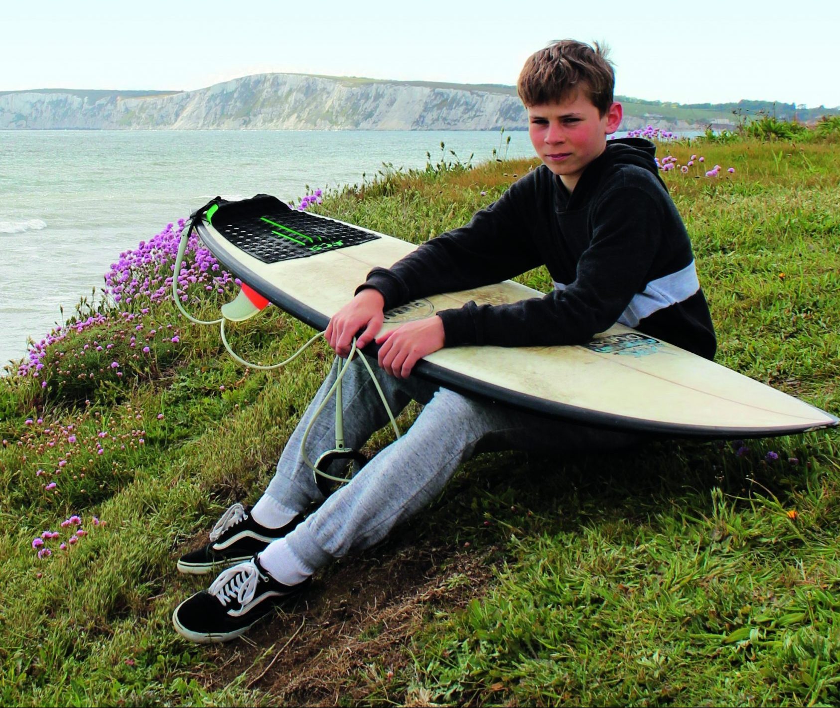 Isle of Wight surfer Jago Tasker sitting on a hill with his surfboard overlooking the coastline