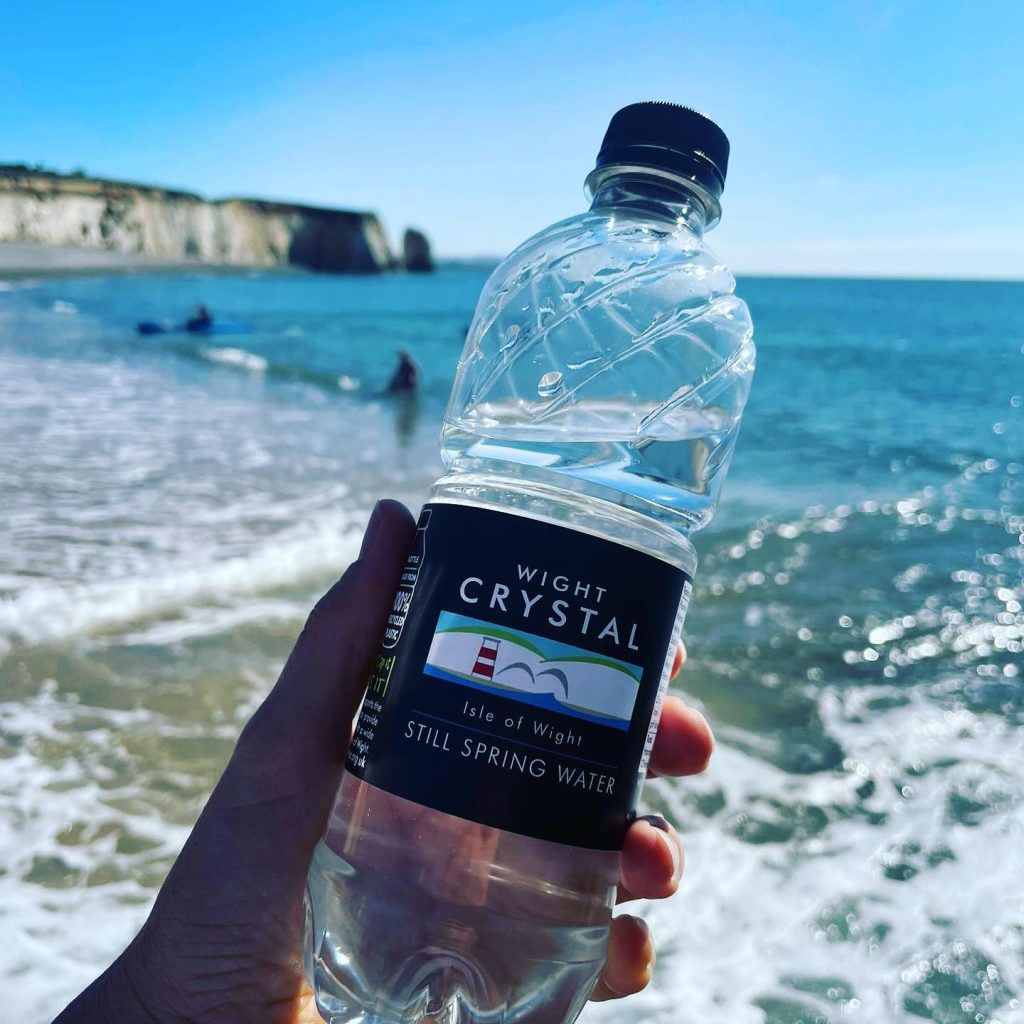 A hand holding a bottle of Wight Crystal water on a beach on the Isle of Wight