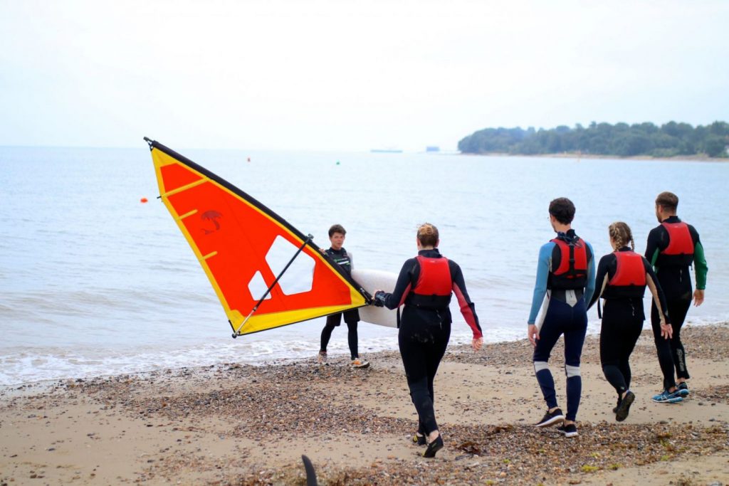 A group of people entering the water to learn to windsurf on the Isle of Wight