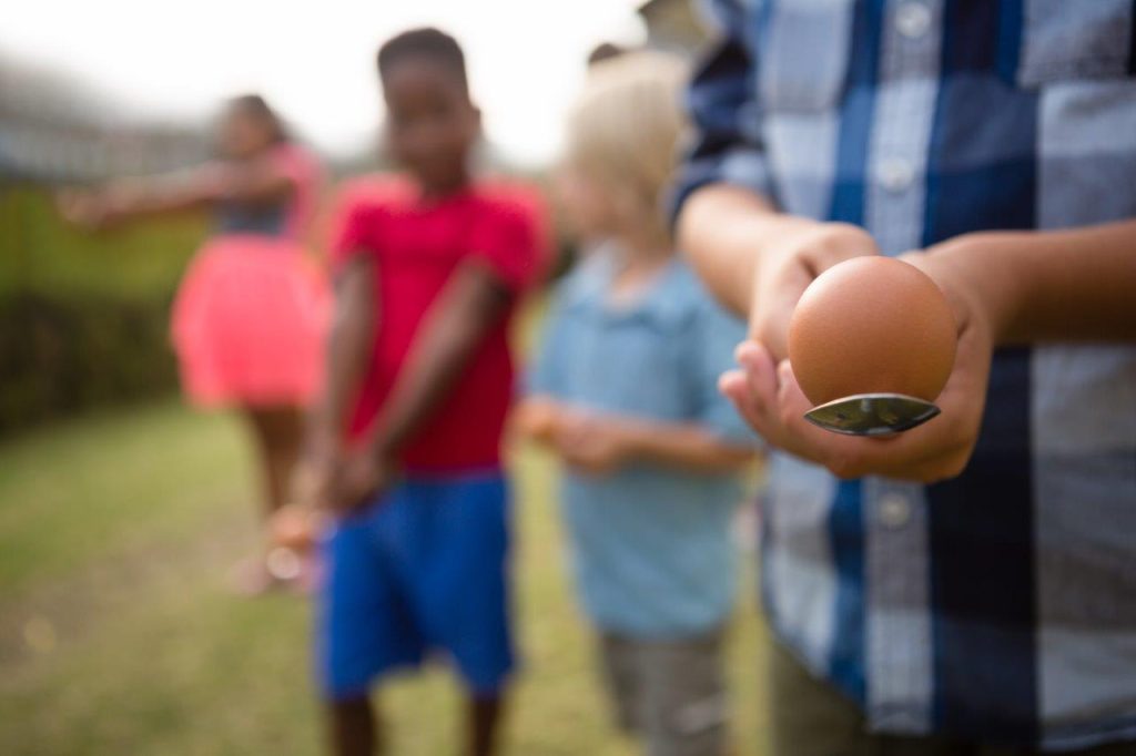 A group of children standing with eggs on spoons waiting for a race outdoors