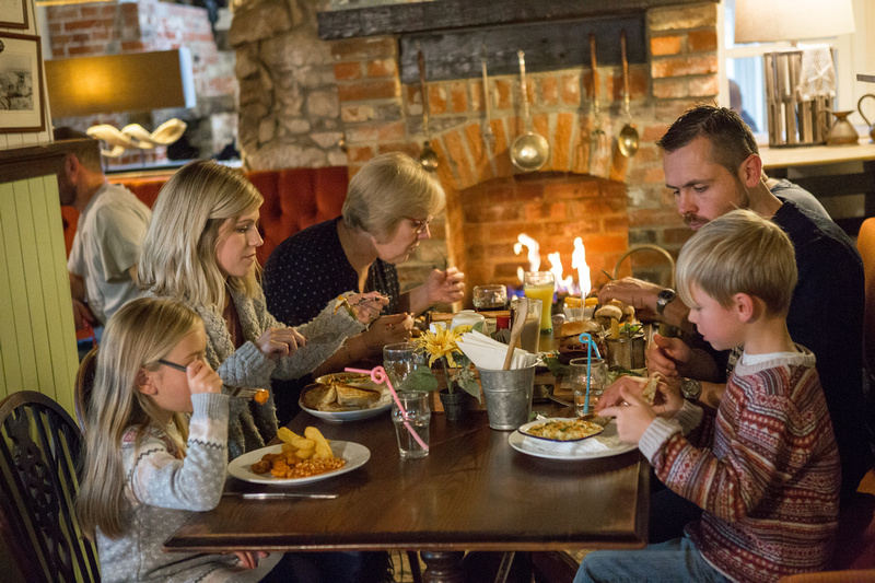 Family of five dining at a pub table by a log fire