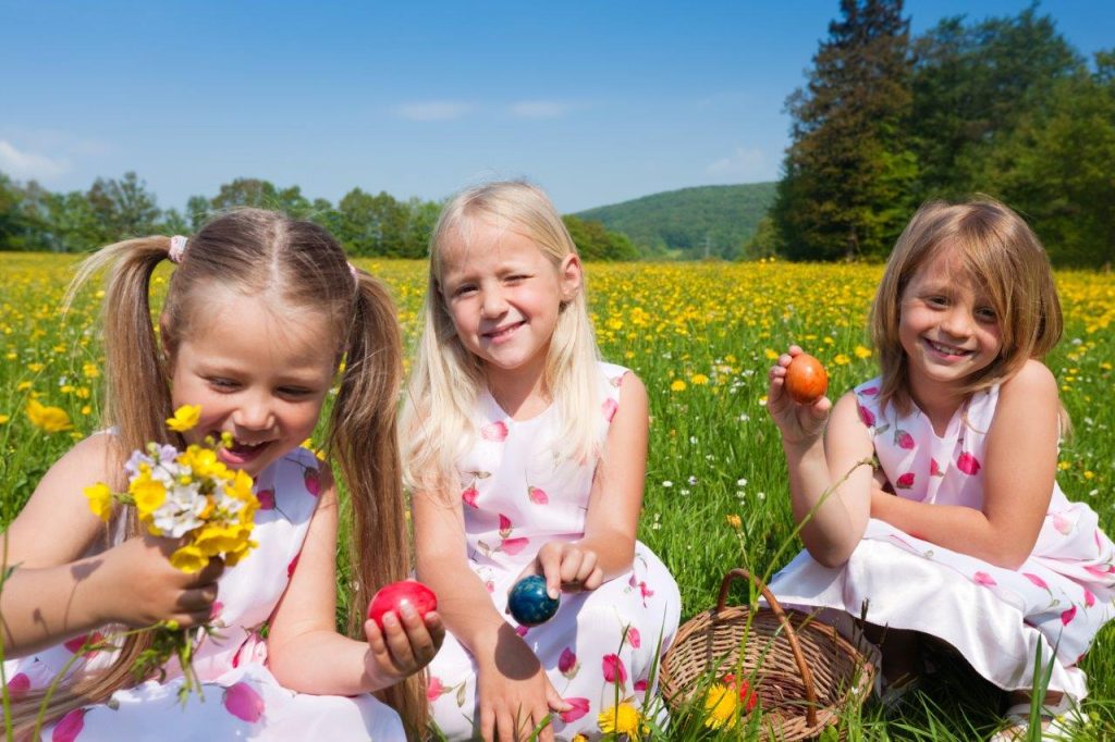 Three children in a field with spring flowers and Easter eggs