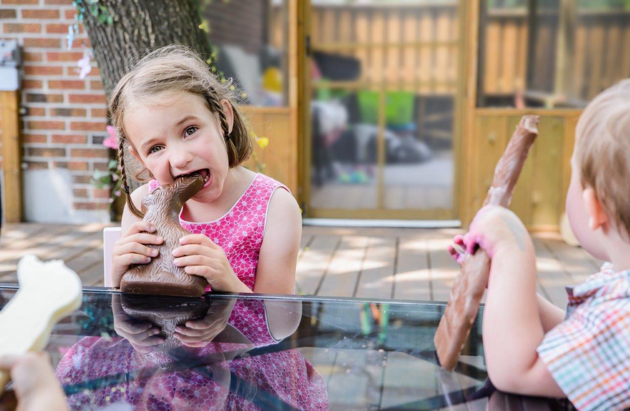 Two children eating chocolate Easter bunnies outside