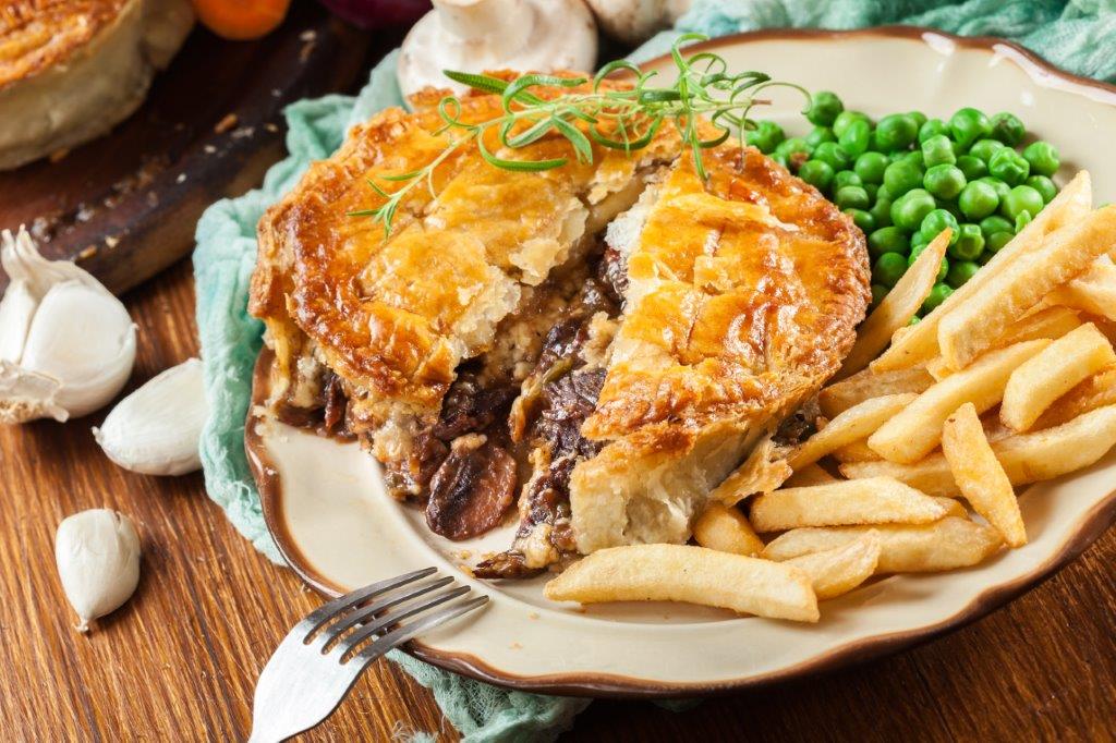 A pie on a white plate with chips and peas