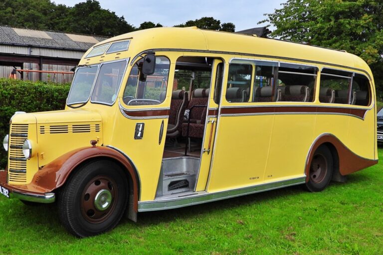 A yellow and brown vintage bus, with a rounded front and large windows. The bus door is open, showcasing the retro interior seating. The vehicle is parked on green grass.