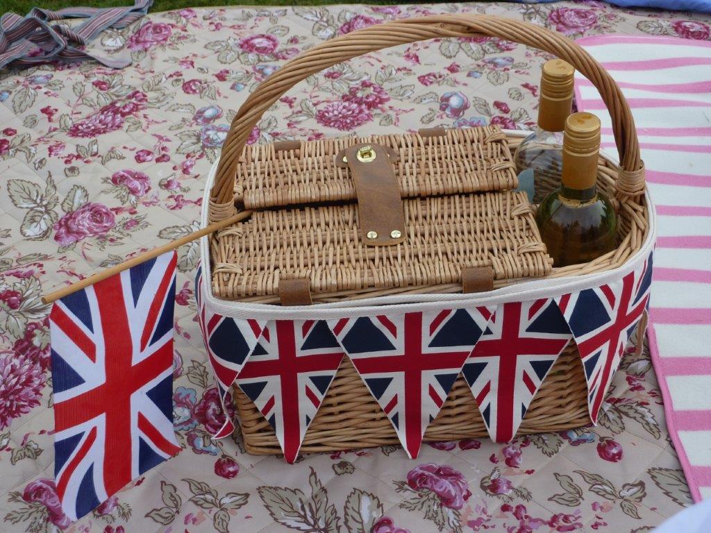 A picnic basket on a floral rug with Union Jack Flags and wine