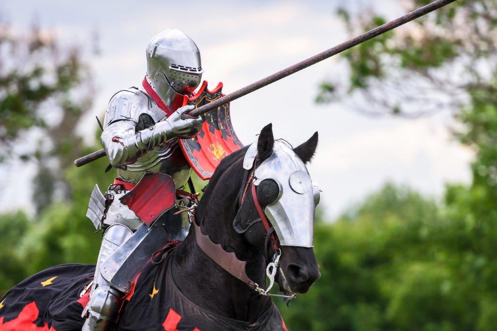 A man in a Medieval knight costume jousting on a horse