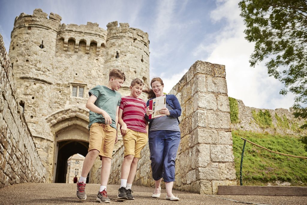 A mother and two children outside Carisbrooke Castle looking at a guide