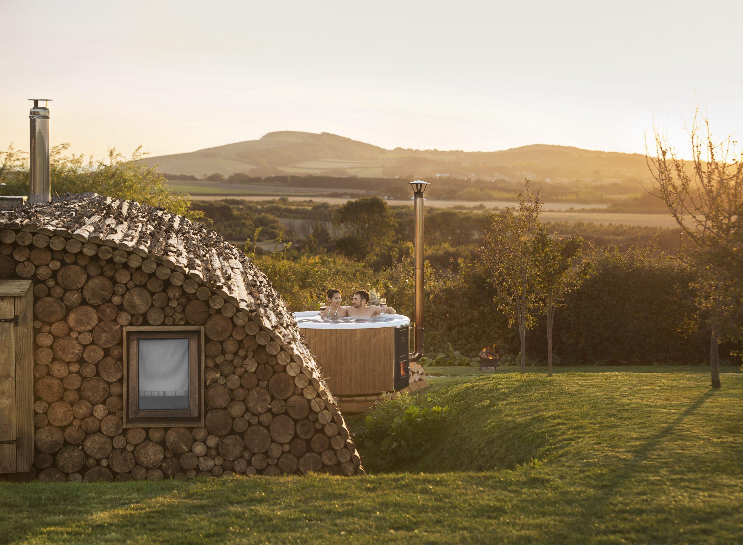 A domed lodge made from logs, overlooking the countryside at sundown. There's a hot tub.