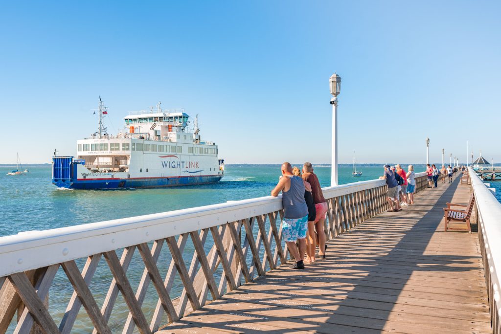 A group in shorts and t-shirts stand on Yarmouth Pier looking out towards the Wight Light Wightlink ferry