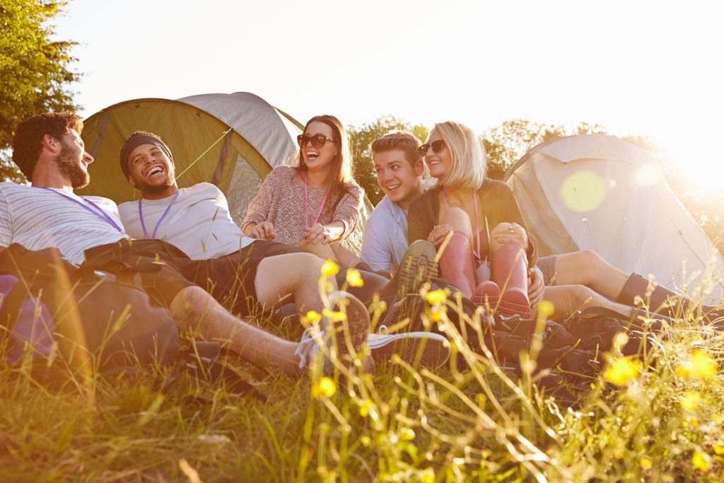 A group of friends in the sunlight and grass laughing next to tents