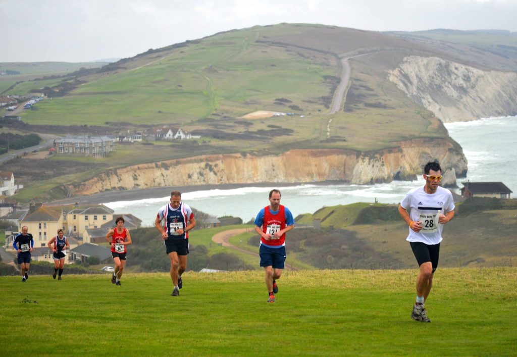 Runners running up a hill on the Isle of Wight with sea and hills behind them