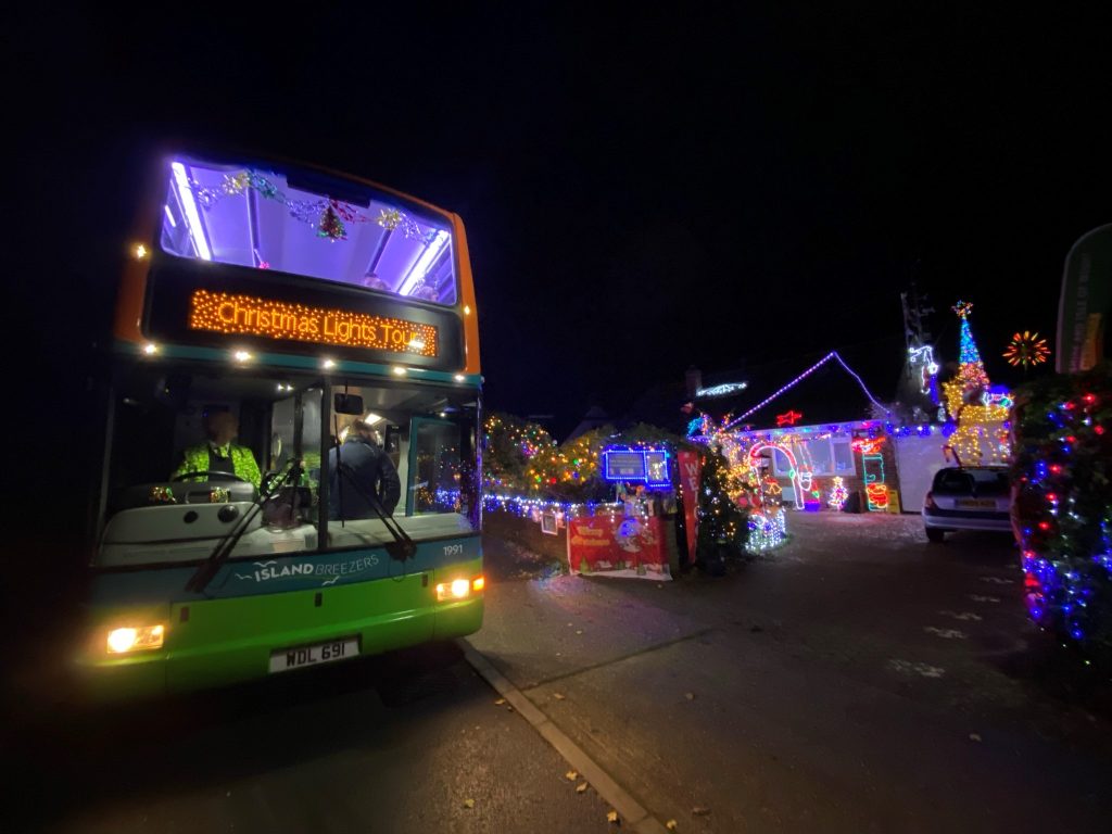 A double decker bus travelling at night next to some Christmas lights on the Isle of Wight