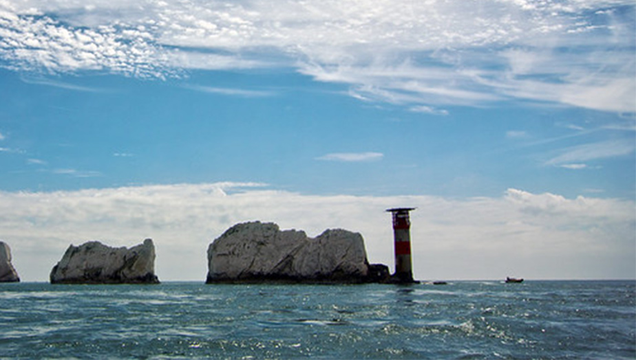 Blue ocean water and blue sky with thin white clouds with the famous Isle of Wight landmark The Needles.