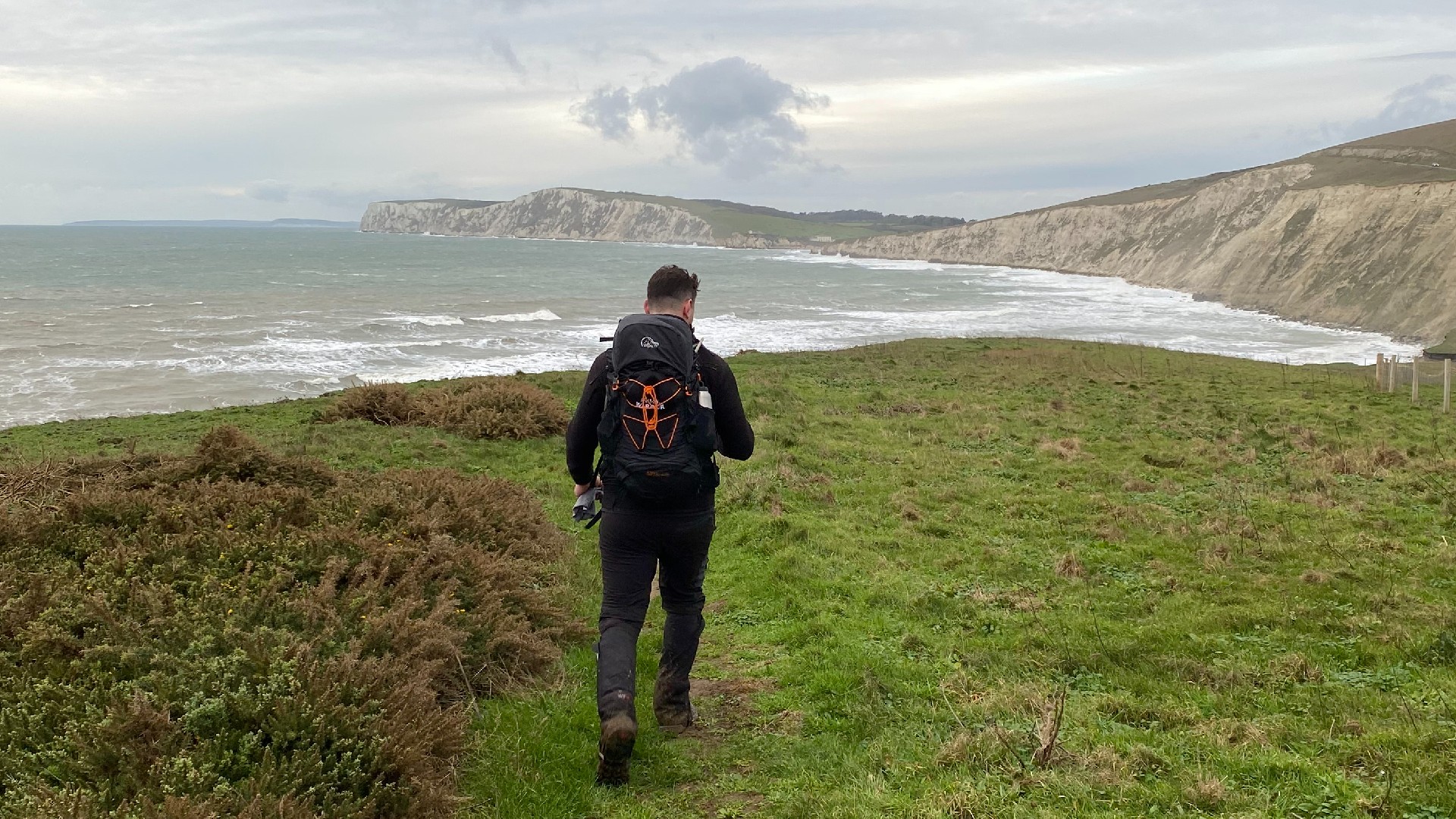 A walker strolls along the Wilder Wight Walking route, with Isle of Wight cliffs in the distance