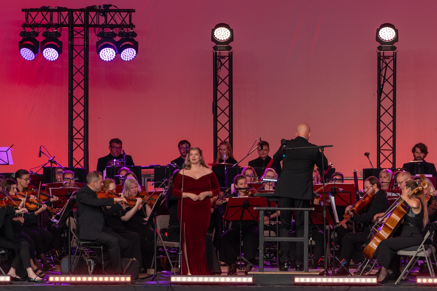 Live orchestra performance on stage with conductor and solo vocalist in evening concert setting under colourful lighting