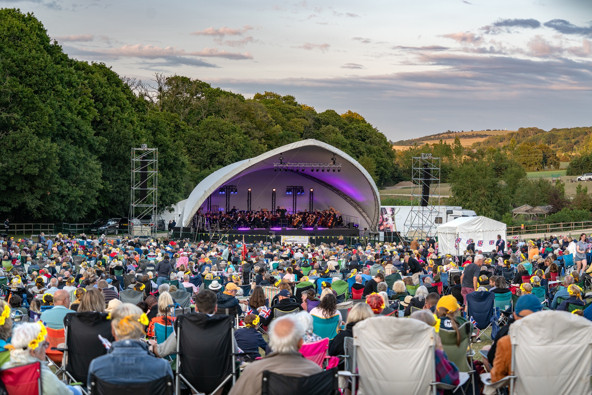 Large outdoor stage at Robin Hill with full orchestra performing to a packed crowd seated on the grass