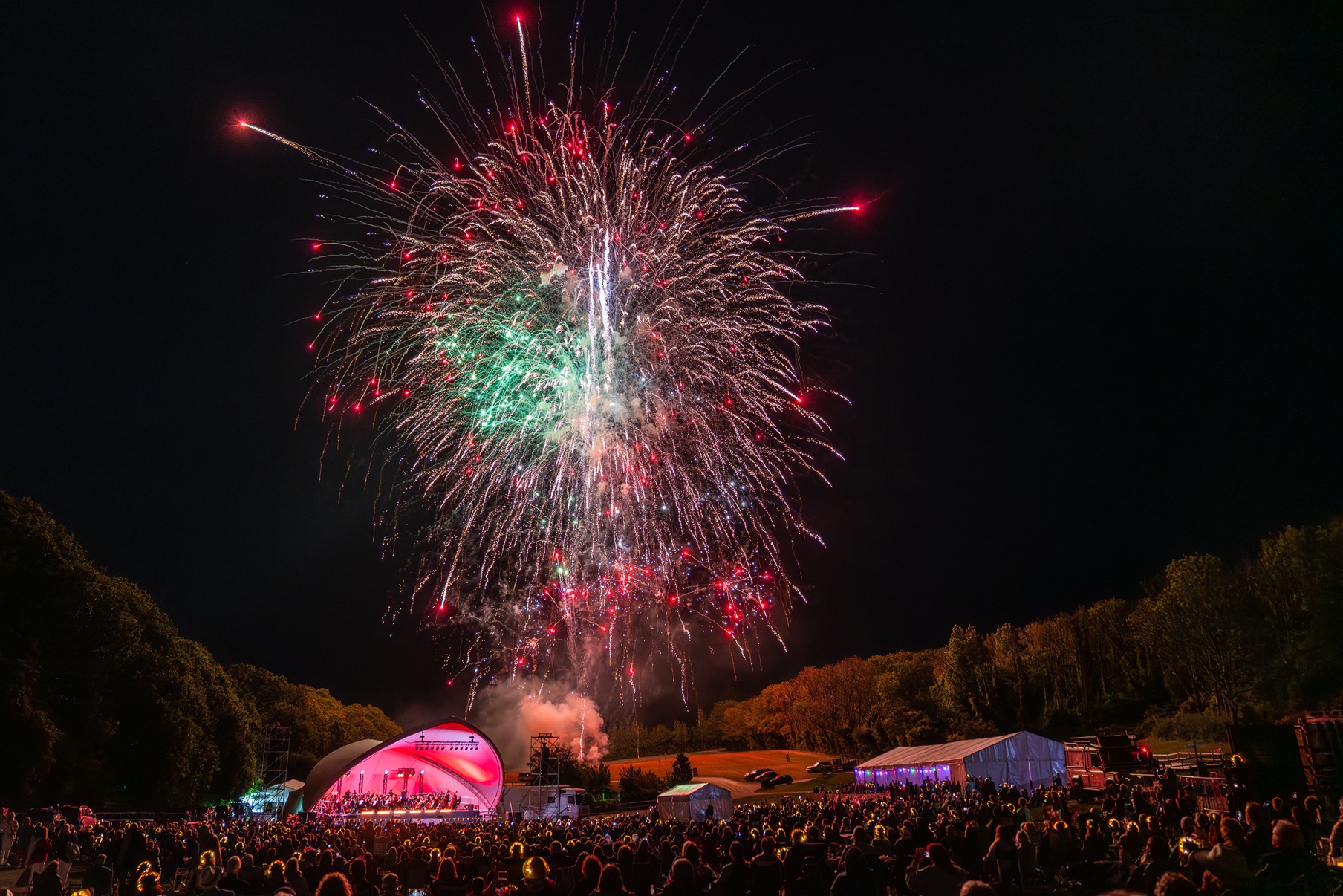 Fireworks lighting up the night sky above an outdoor Proms stage, with a large crowd watching the finale concert at Robin Hill
