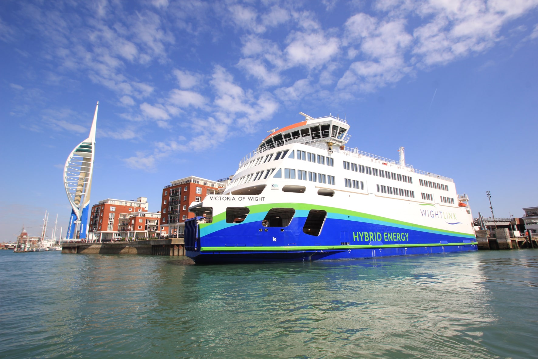 A large ferry, coloured white with blue and green stripes, in the water outside Portsmouth with the Spinnaker Tower in the background
