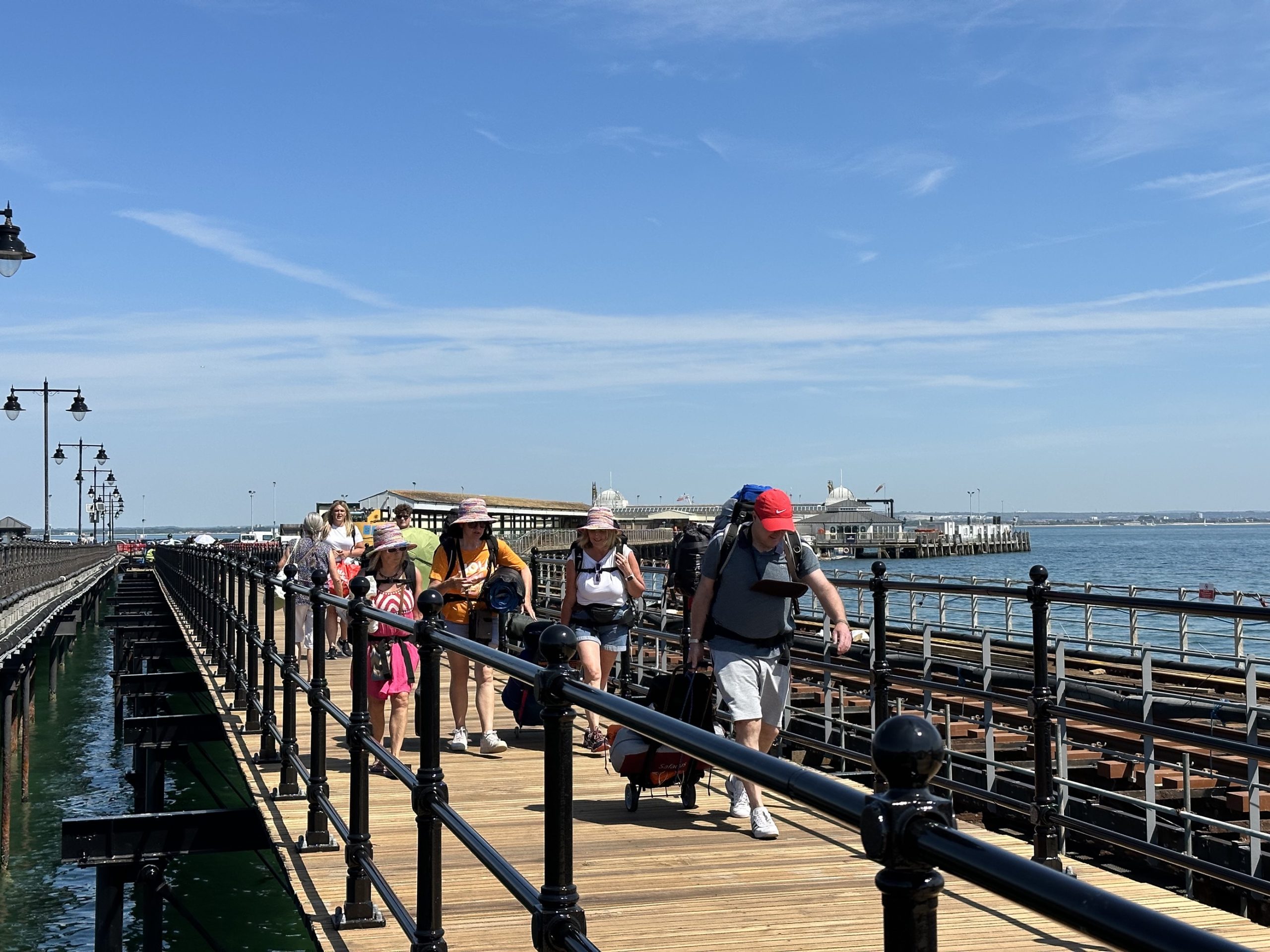 People walking down a pier footway dressed in summer clothes and carrying luggage