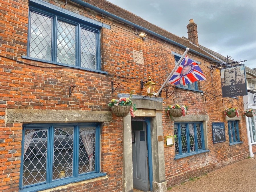The exterior of The Castle Inn, Isle of Wight - a red brick two storey building with blue window frames, hanging baskets and a union jack flag