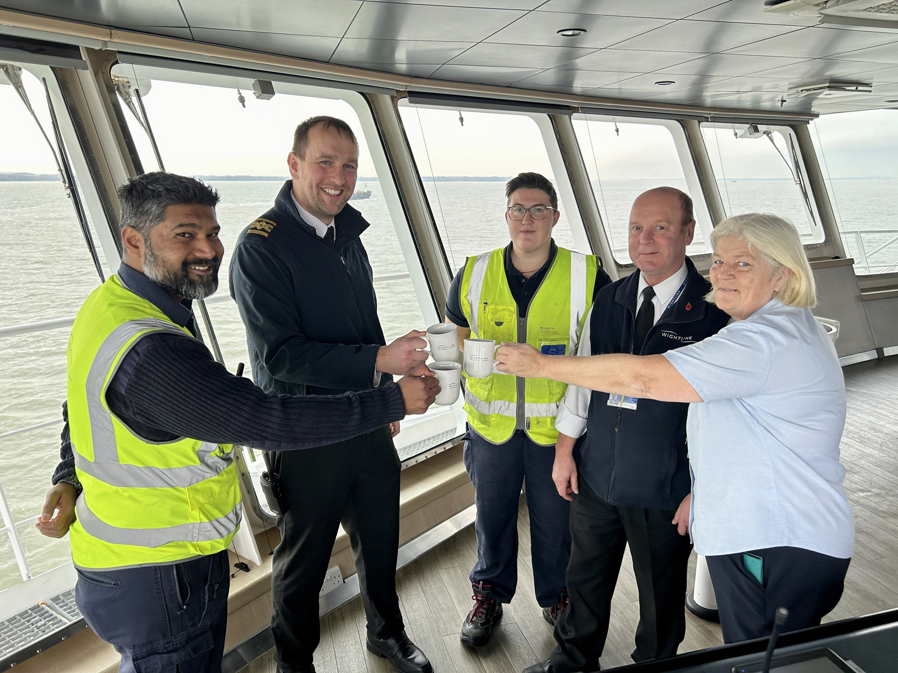 Wightlink employees standing in a circle raising a toast with cups of tea onboard the Victoria of Wight ferry