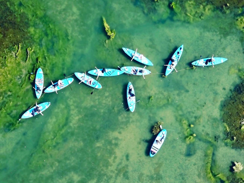An aerial shot of a collection of stand up paddleboards on a river with people doing yoga on them