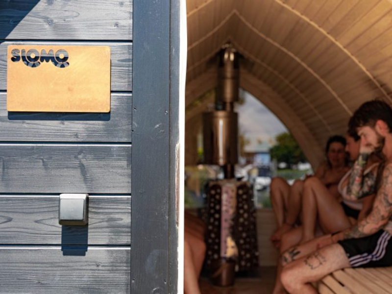 A shot of a sauna taken from the outside looking in. It's made of wood and has a domed ceiling. People are sitting inside in swimwear