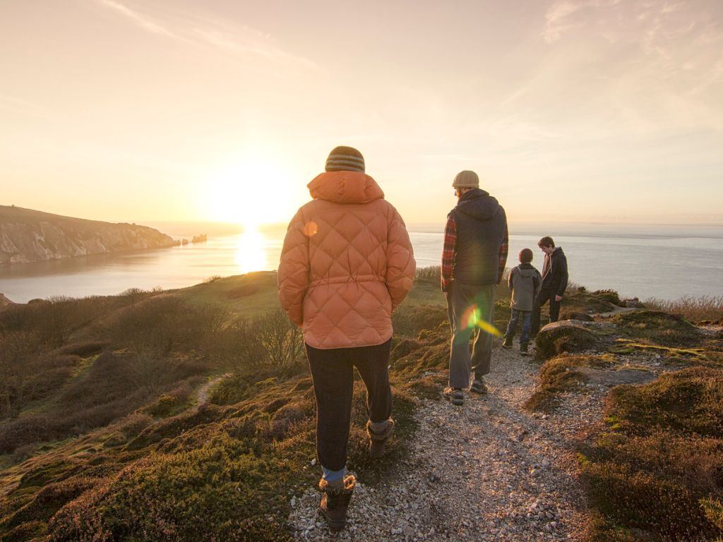 A family walking during the winter on Headon Warren, overlooking The Needles on the Isle of Wight, with the sun setting