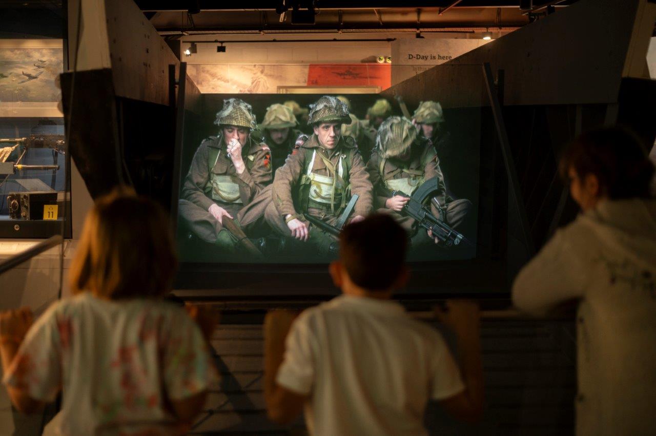 Three children watching a projector screen with soldiers from WWII