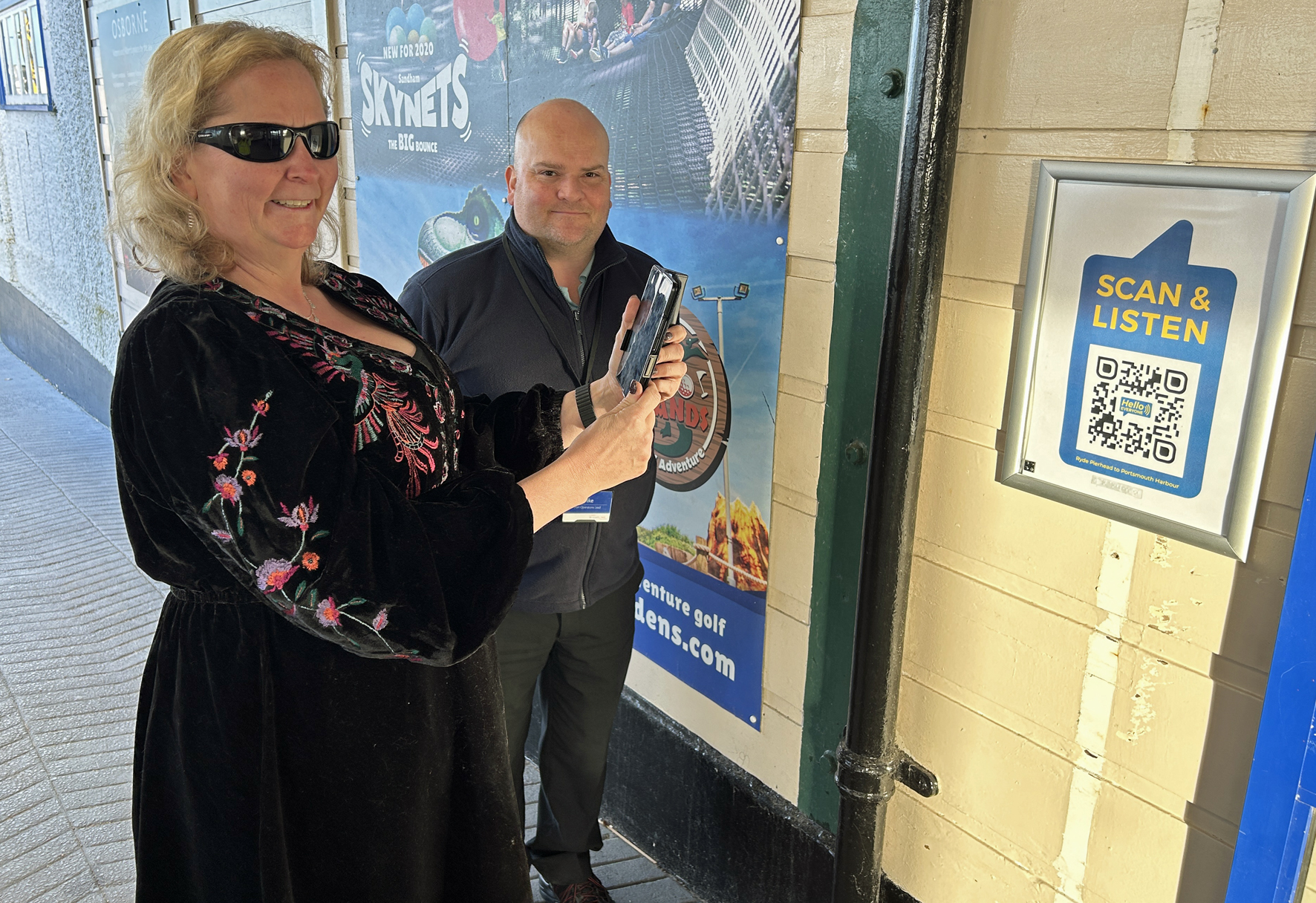 Two people using a phone to scan a QR code that gives an audio and video description of the layout of Wightlink ferry terminal