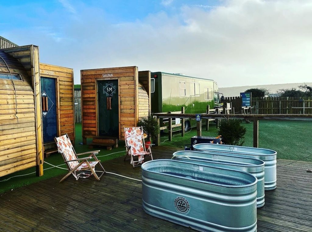 Two metal ice baths in front of two wooden saunas with deck chair seating
