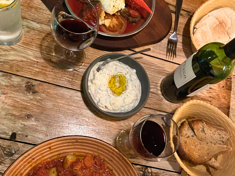 Mediterranean food, including hummus, with wine and bread on a wood table