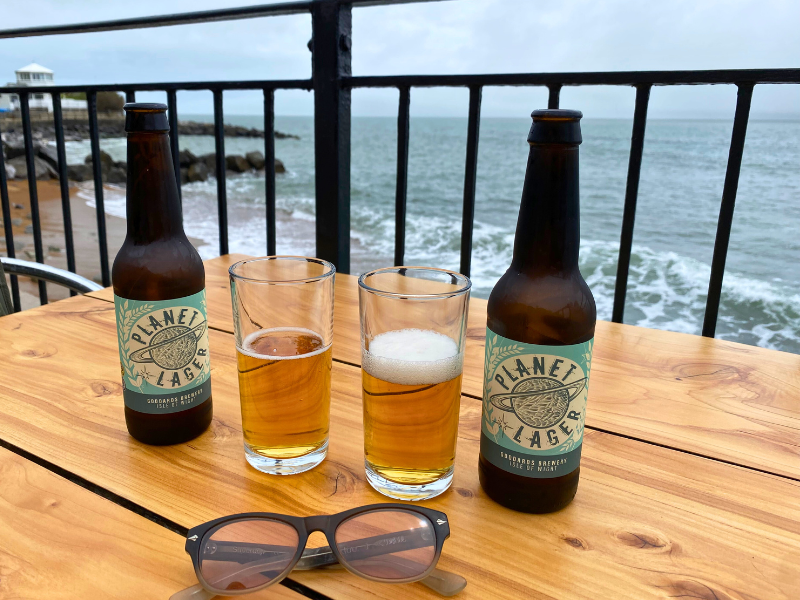 Two beer bottles and glasses on a wood table overlooking the sea